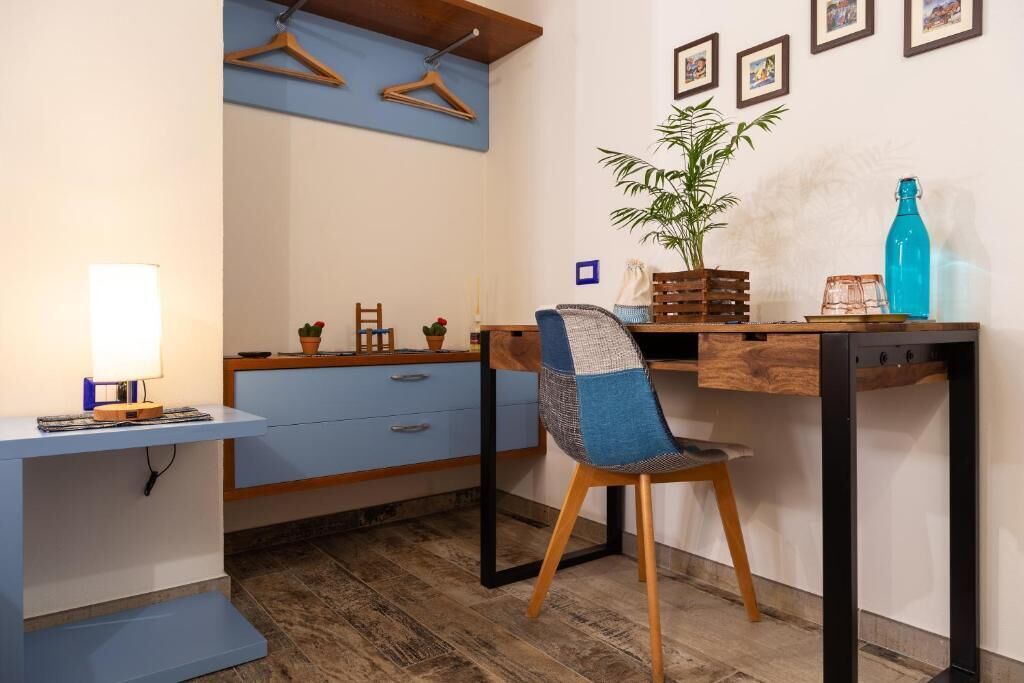 Una habitación con escritorio, silla, lámpara y estantes en la pared.