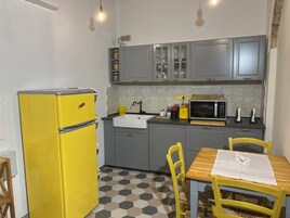 Una cucina compatta con un frigorifero giallo, mobili grigi, un forno a microonde e un tavolo da pranzo in legno con sedie.