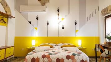 Ein Schlafzimmer mit Gelb-Weiß-Farbgebung, einem Bett mit Bettdecke in geometrischem Muster, Nachttischlampen und einer Wand-Klimaanlage.