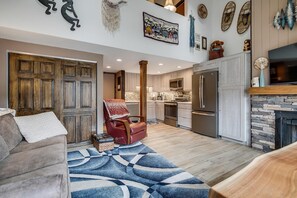A spacious living area with a large wooden door, a leather armchair, a blue patterned rug, and a kitchen with modern appliances. - Der Steiermark 219 in Breckenridge (Breckenridge)