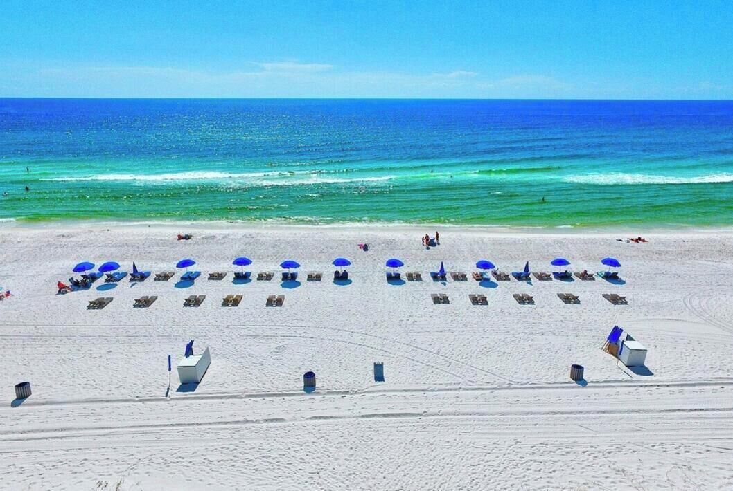 En strand med rader av solstolar och parasoller, en klarblå himmel och havet i bakgrunden.
