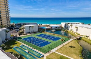A tennis court surrounded by buildings, a pool, and a view of the ocean. - BEACHFRONT COMPLEX, 2nd-Floor, park next to unit, steps to pool/wide open beach (Panama City Beach)