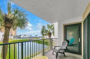 A balcony with a view of a water body and palm trees, a sliding glass door, and a chair. - BEACHFRONT COMPLEX, 2nd-Floor, park next to unit, steps to pool/wide open beach (Panama City Beach)