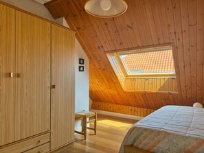 Ein Schlafzimmer mit schrägverdeckter Decke, Holzwänden, einem Oberlicht, einem Bett und einem Kleiderschrank.