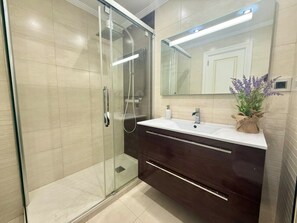 A modern bathroom with a glass shower enclosure, a dark wooden vanity, and a mirror above the sink. - Tutto Bene Apartment 6906 (Helgueras)