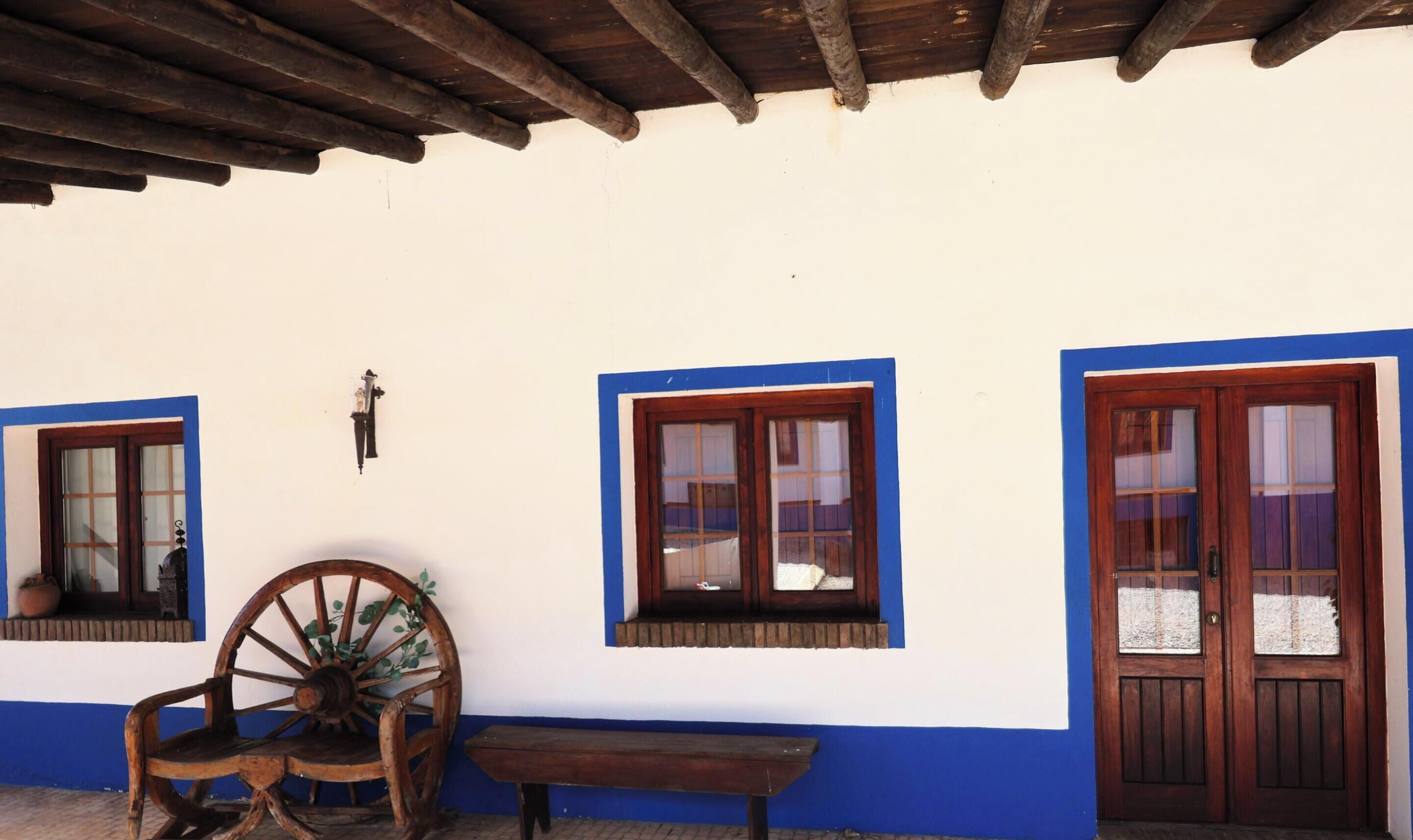 A rustic building with a wooden porch, a large wooden wheel, and a bench.