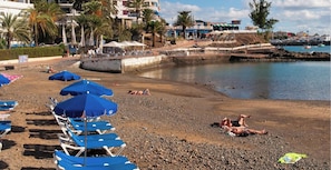 A beach with sun loungers and umbrellas, a rocky shoreline, and a marina in the background. - Maranuelas 308 by VillaGranCanaria (Arguineguin)