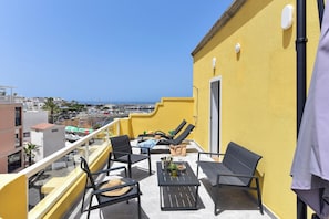 A balcony with outdoor furniture, a view of the sea, and a yellow building. - Maranuelas 308 by VillaGranCanaria (Arguineguin)