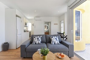 Een moderne woonkamer met een grijze bank, een bijzettafeltje en een eethoek op de achtergrond.