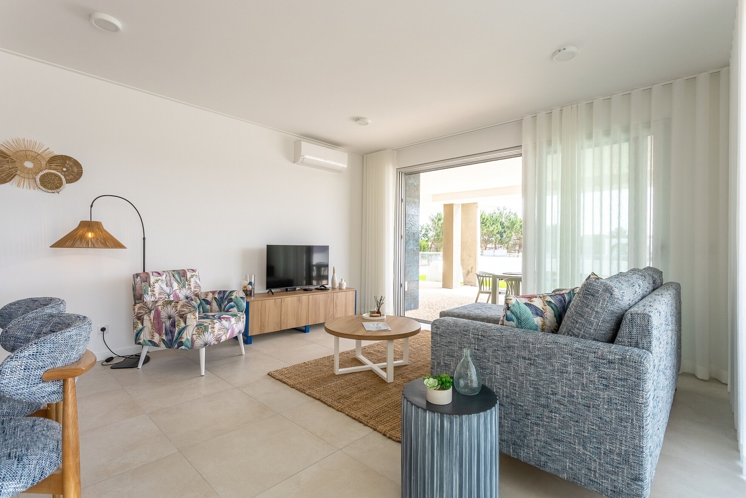 A modern living room with a sofa, armchair, TV, and a dining area with a table and chairs.