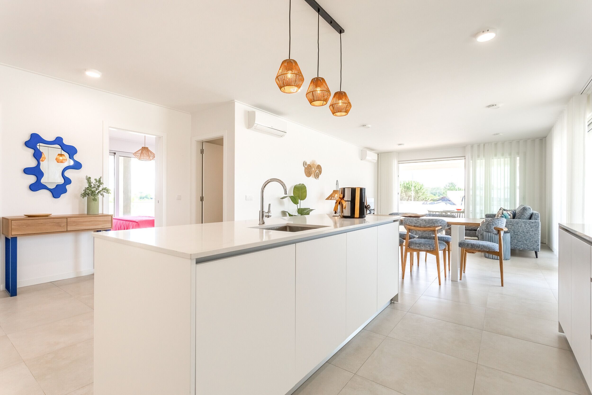 A modern kitchen with a central island, pendant lights, and a dining area with chairs and a table.