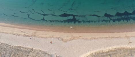 An aerial view of a beach with clear water, sandy shore, and sparse vegetation.