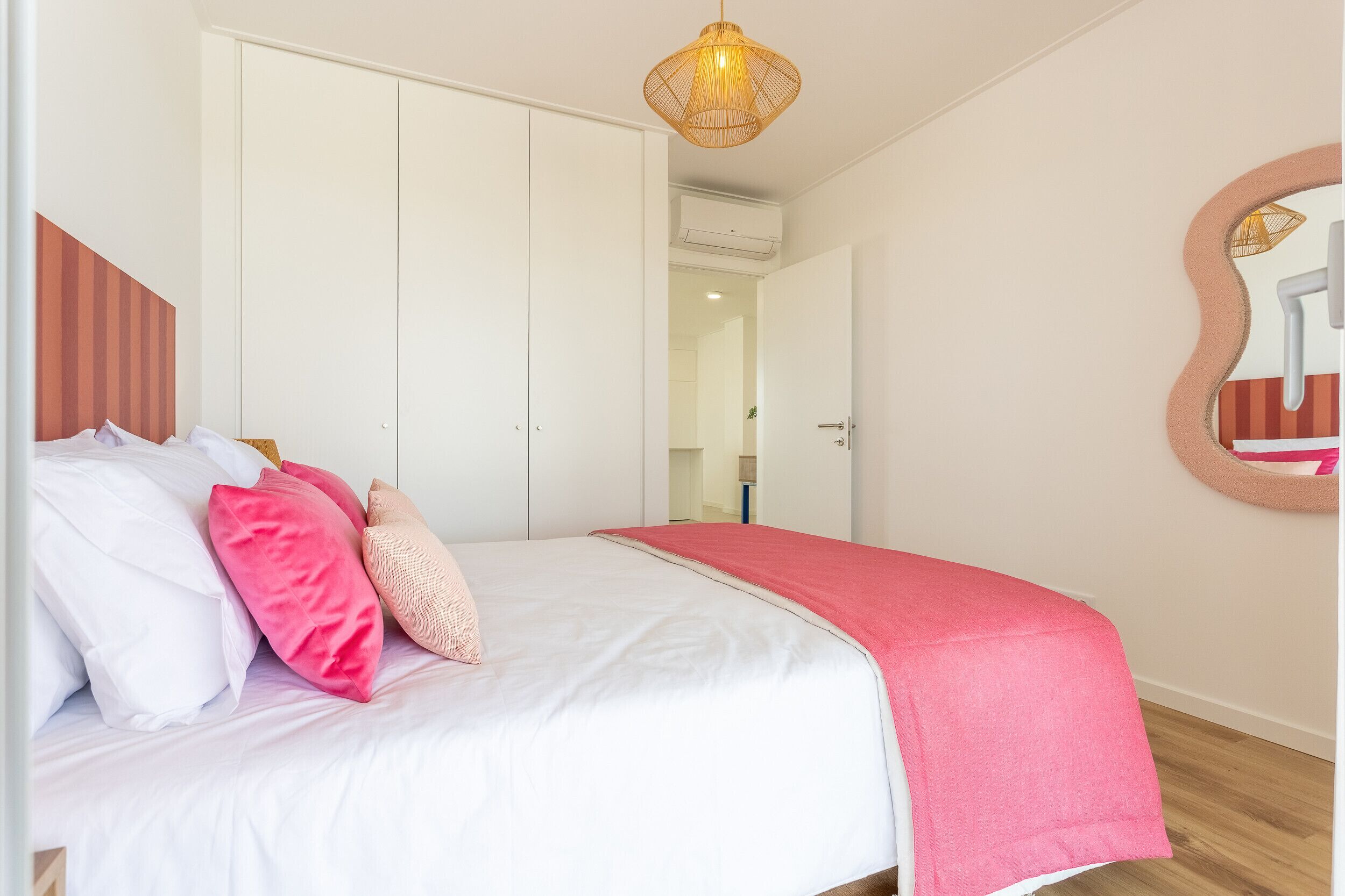 Une chambre à coucher avec un lit, des oreillers, un luminaire suspendu et un miroir au mur.