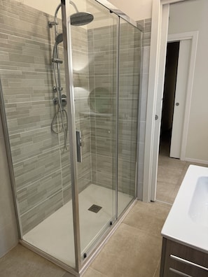 Ducha con cerramiento de vidrio, cabezal de ducha de mano y llave de pared.