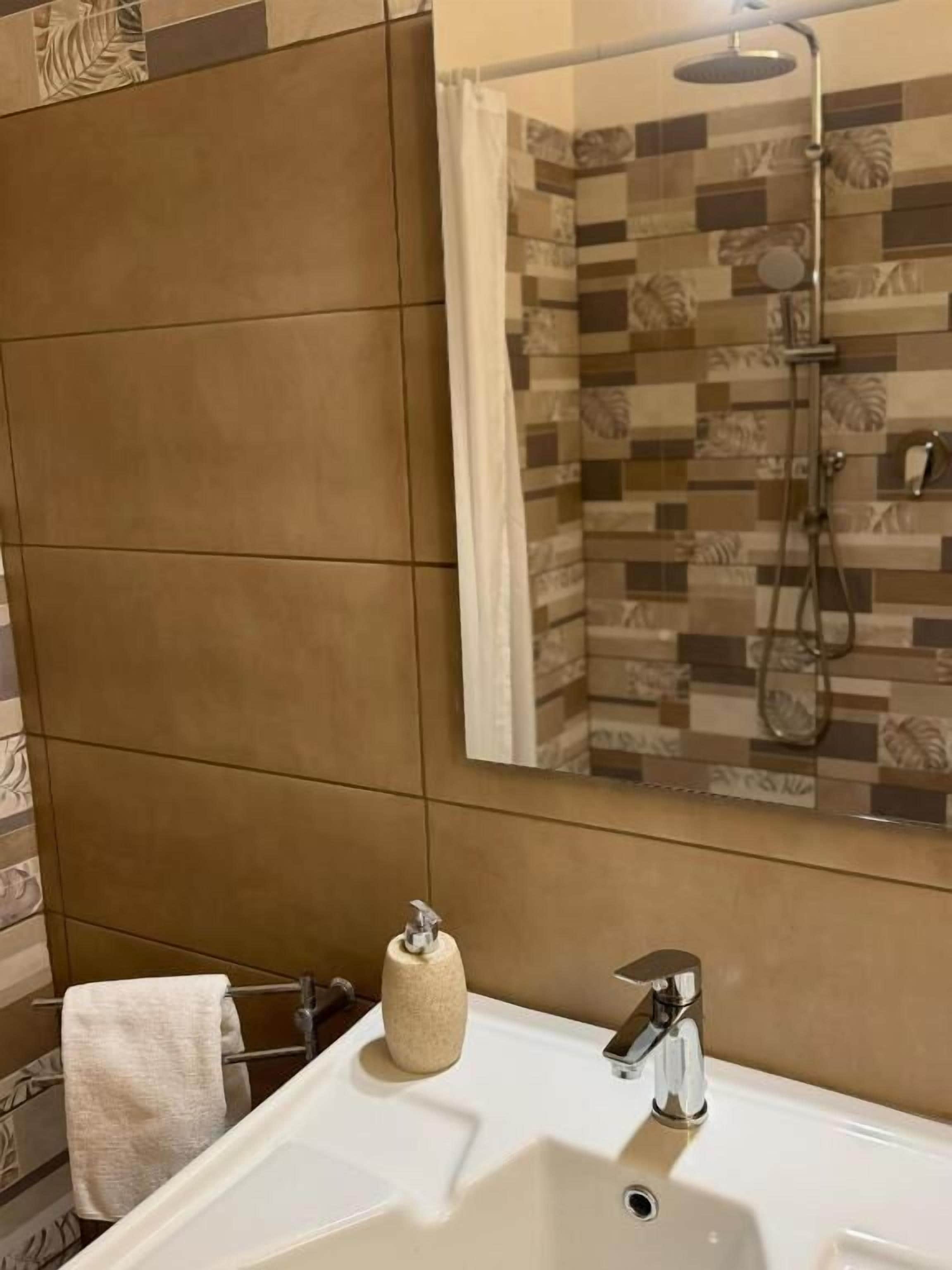 A bathroom with a white sink, a towel rack, and a shower with a tiled wall.