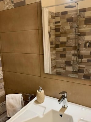 Un baño con un lavamanos blanco, un perchero y una ducha con pared de azulejos.
