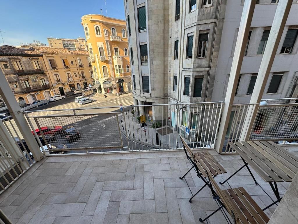 Un balcon donnant sur une rue de la ville, avec une rambarde en métal et un banc en bois.