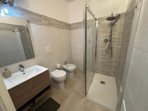Un bany modern amb dutxa amb envidriera, un lavabo, un vàter i un bidet.
