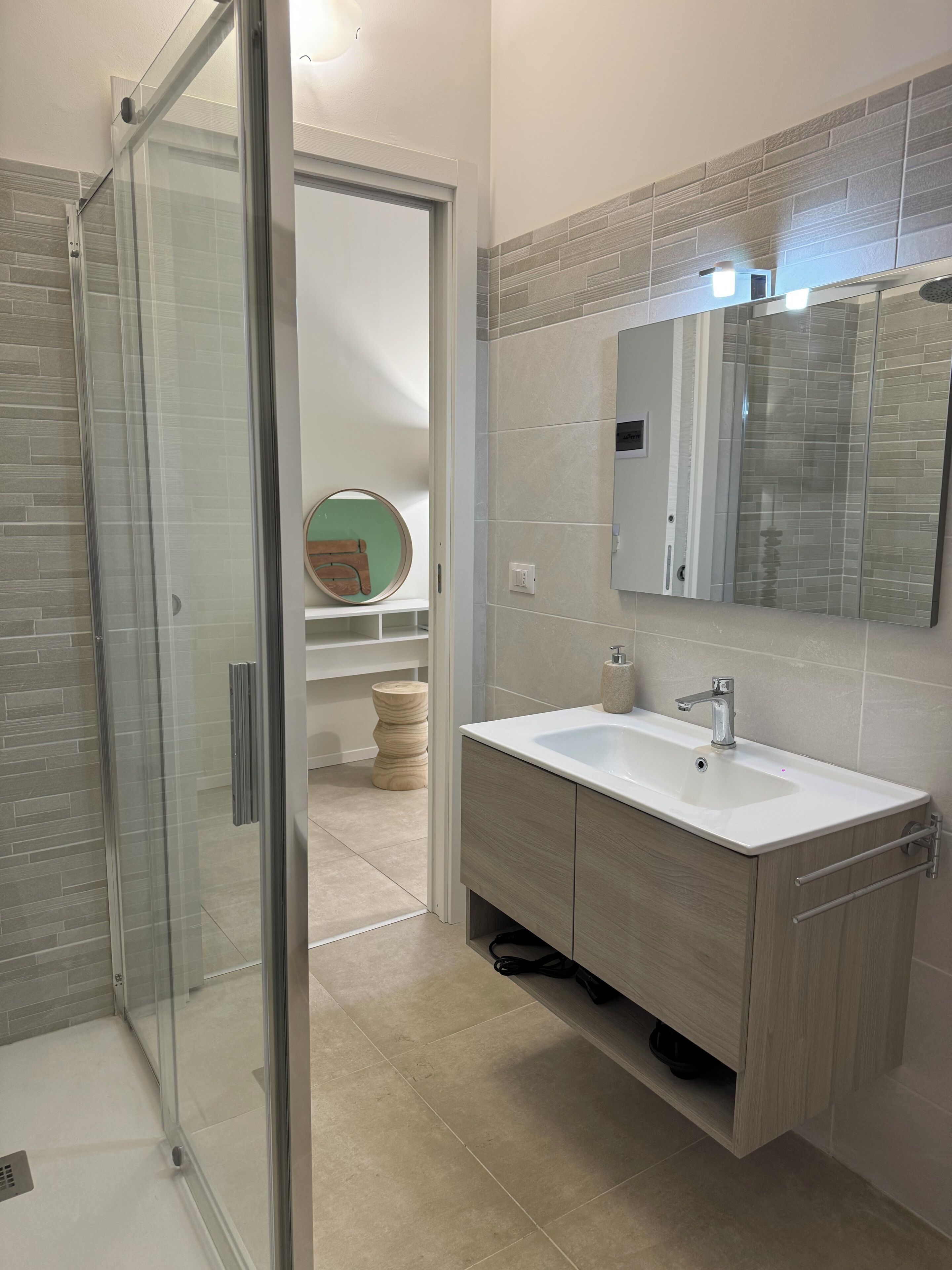 Une salle de bain moderne avec une douche à parois de verre, un lavabo avec un miroir au-dessus et un meuble-lavabo en bois.