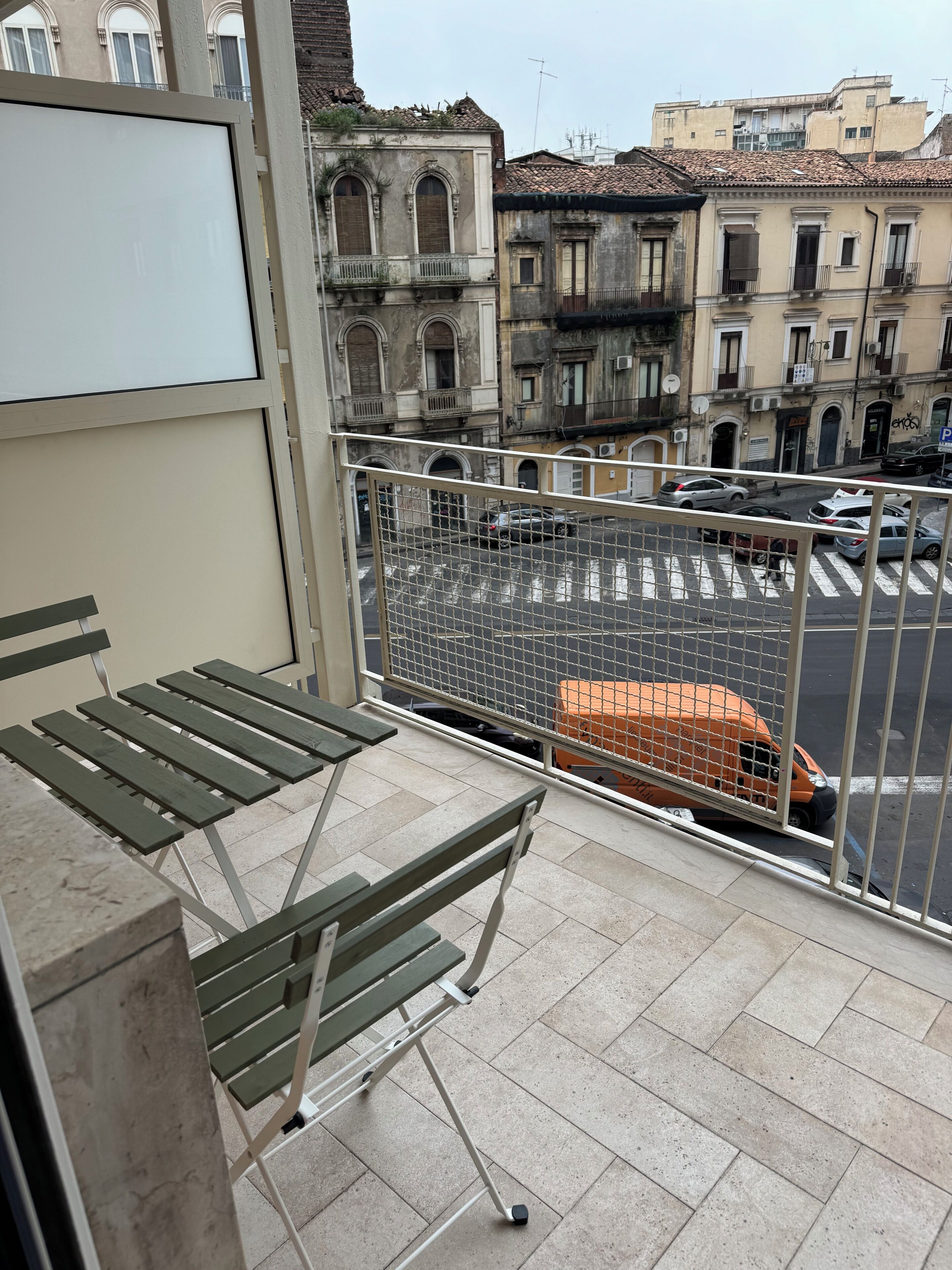 A balcony with a metal railing, a folding table, and a view of a street with parked cars and buildings.