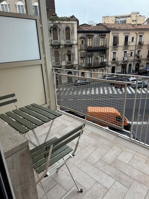 Un balcón con barandilla de metal, una mesa plegable y vista a una calle con coches estacionados y edificios.
