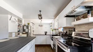 A modern kitchen with white cabinetry, a black countertop, and stainless steel appliances. - Spacious 4-bedroom house in welcoming Thornton, Cozy for families to relax. (Thornton)