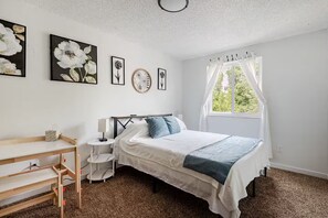 Ein Schlafzimmer mit Bett, Nachttischen, Schreibtisch und einem Fenster mit Vorhängen.