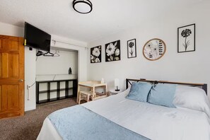 Une chambre à coucher avec un lit, un bureau, une télévision et des œuvres d’art accrochées au mur.