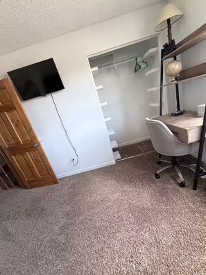 A room with a wooden door, a flat-screen TV mounted on the wall, a desk with a lamp, and a globe. - Spacious 4-bedroom house in welcoming Thornton, Cozy for families to relax. (Thornton)