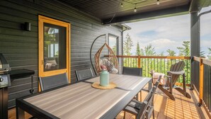 Een houten terras met een tafel, stoelen, een hangstoel en een barbecue.