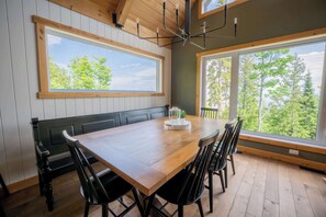 A dining area with a wooden table, black chairs, a bench, and a chandelier. - Shack Saison - St-Lauwrence River (Petite-Rivière-Saint-François)
