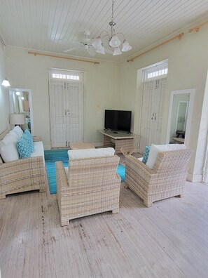 A room with wicker furniture, a ceiling fan, and a television. - Clariston - Traditional Barbadian home 1 minute walk from beach! (Oistins)
