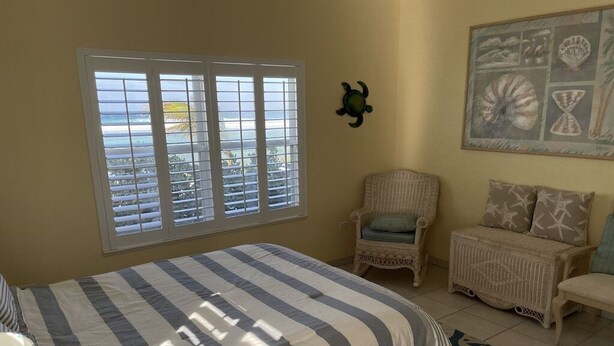 Um quarto com cama, janela com persianas, uma cadeira, um sofá e um quadro na parede.