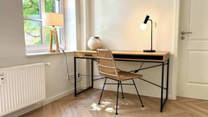 A corner workspace with a desk, chair, lamp, radiator, and window with curtains. - Warnemünder Auszeit 2 (Rostock)