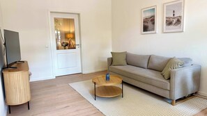 Un salon comprenant un canapé, une table basse, un téléviseur posé sur un meuble et deux tableaux encadrés accrochés au mur.