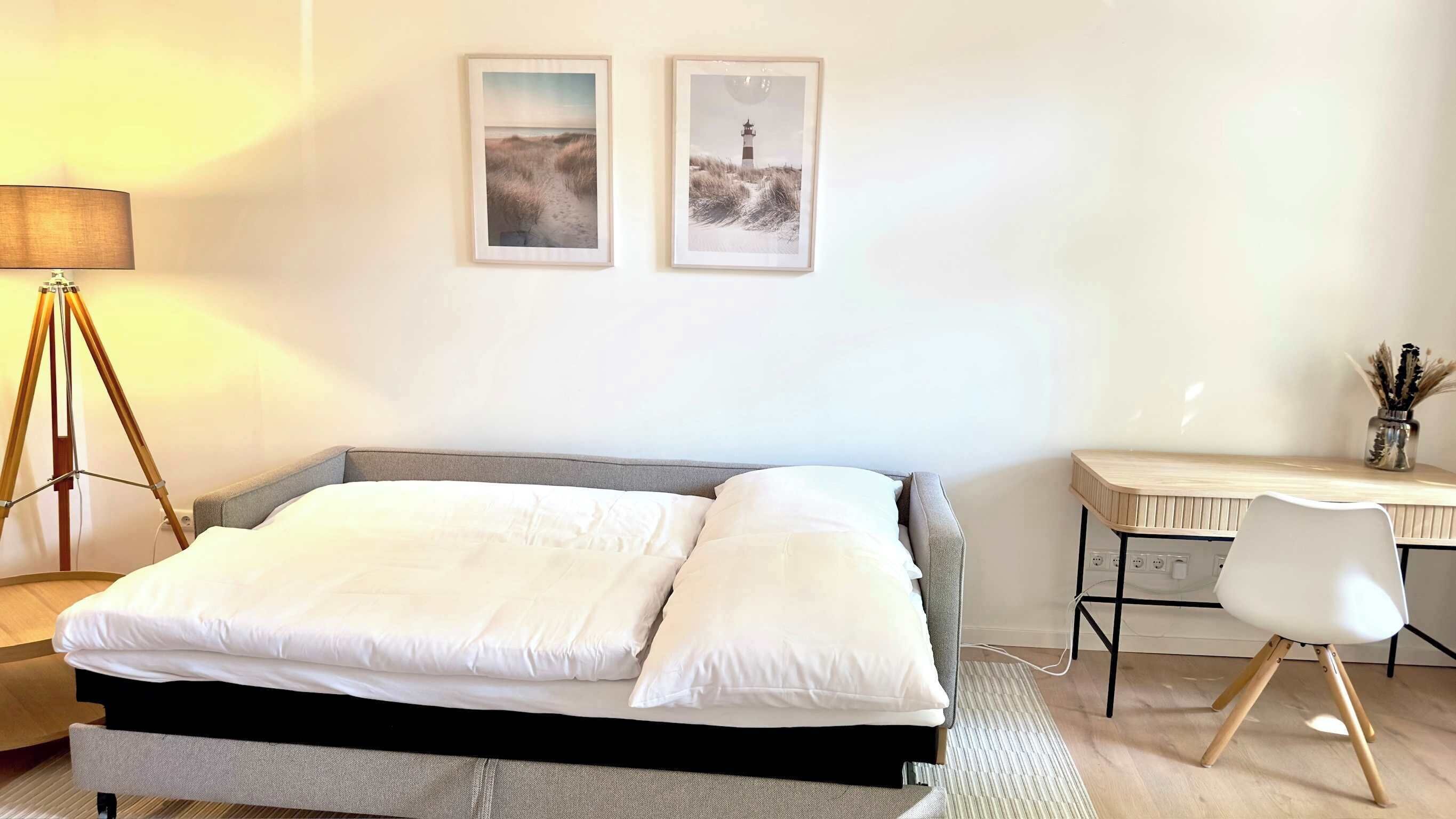 A bedroom with a bed, a desk, and two framed pictures on the wall.