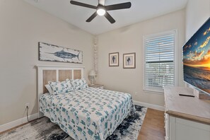 A bedroom with a bed, a ceiling fan, a nightstand, a lamp, a window with blinds, and a wall-mounted TV. - Blue Tide Waterfront Pool & Hot Tub 2 En Suites (Cape Coral)