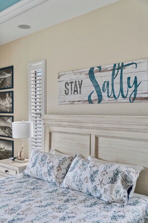 Une chambre à coucher avec un lit, un panneau fixé au mur, une fenêtre avec des stores et un tableau encadré.