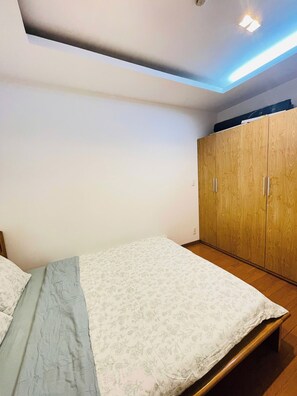 A bedroom with a bed, wooden wardrobe, and a ceiling light fixture. - 2-Bedroom apartment near the airport (Ho Chi Minh City)