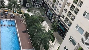 A high-rise residential building with a rooftop swimming pool, palm trees, and a pedestrian walkway.