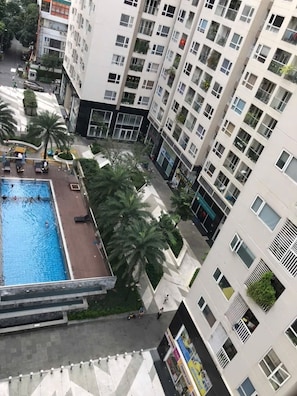 A high-rise residential building with a rooftop swimming pool, palm trees, and a pedestrian walkway. - 2-Bedroom apartment near the airport (Ho Chi Minh City)