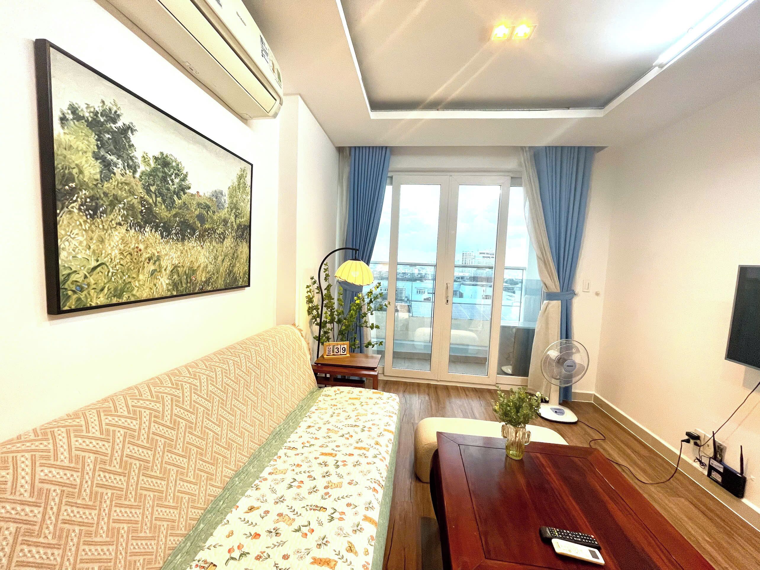 A room with a sofa, a table, a fan, and a window with curtains.