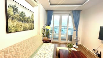 A room with a sofa, a table, a fan, and a window with curtains.