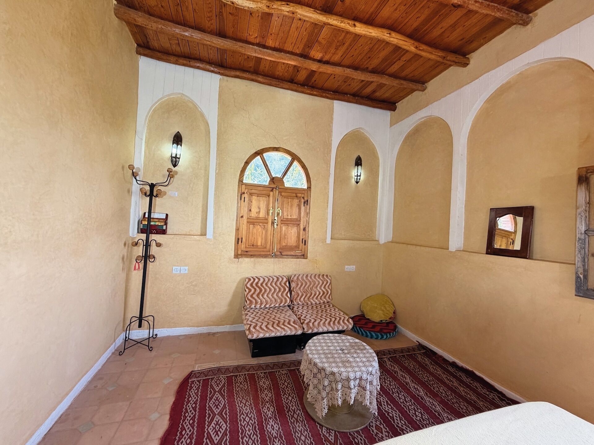 A room with a wooden ceiling, a sofa, a patterned rug, and a small table with a lace tablecloth.