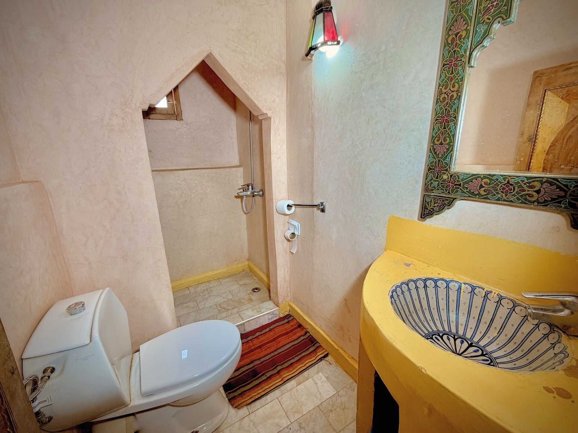 Un baño con inodoro, ducha, lavamanos y un espejo decorativo.
