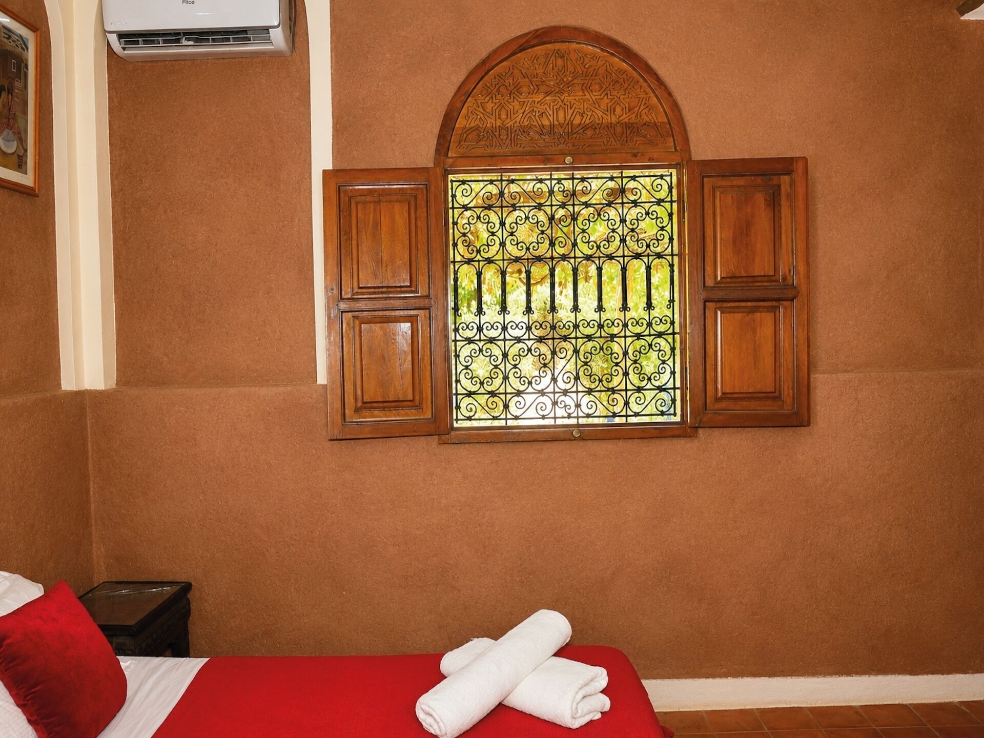 A room with a bed, a window with decorative iron bars, and a wall-mounted air conditioner.