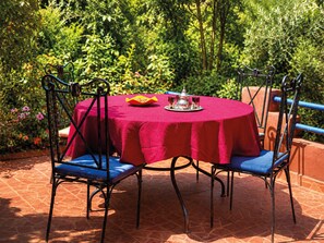 A round table with a red tablecloth, two blue cushioned chairs, and a silver teapot with cups on a tray. - Riad Belgika (Ourika)