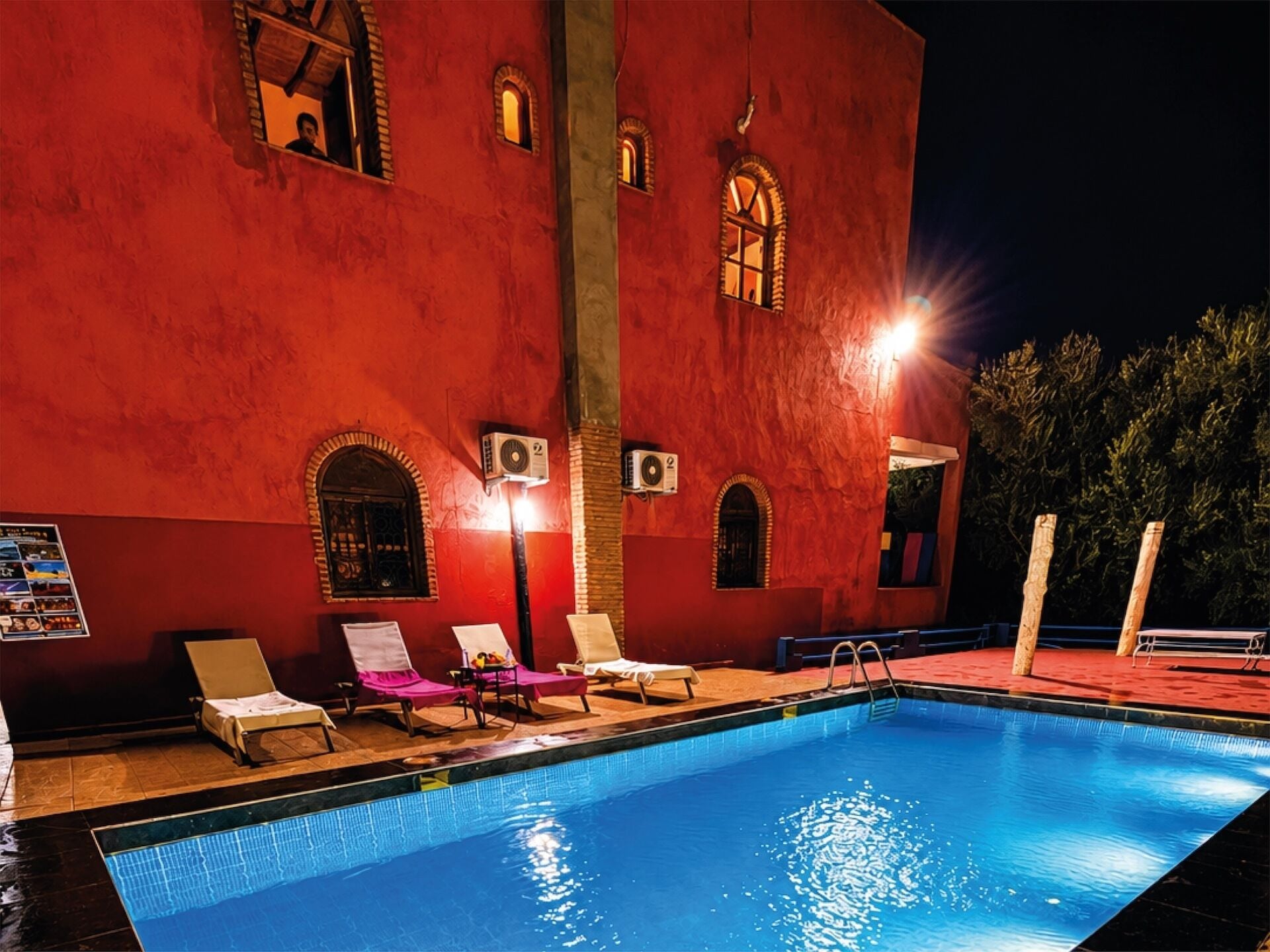 A swimming pool with lounge chairs and air conditioning units on a building facade at night.