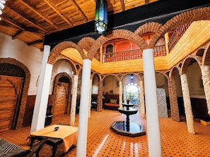 Un interior espaiós amb bigues de fusta, sostres arquejats i una font central.
