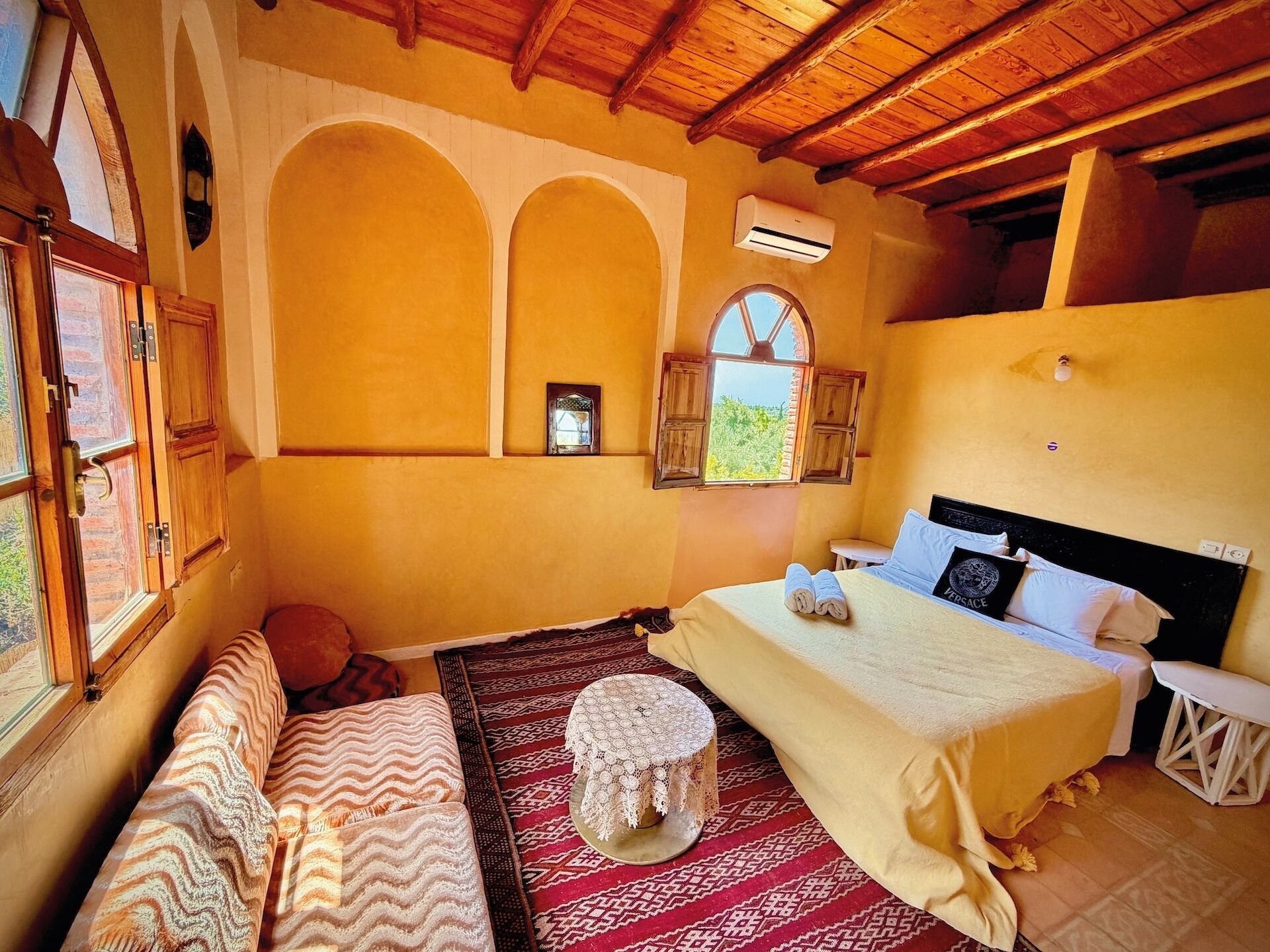 Une chambre à coucher comprenant un lit, un banc, une petite table, un appareil de climatisation et une fenêtre donnant sur un beau paysage.
